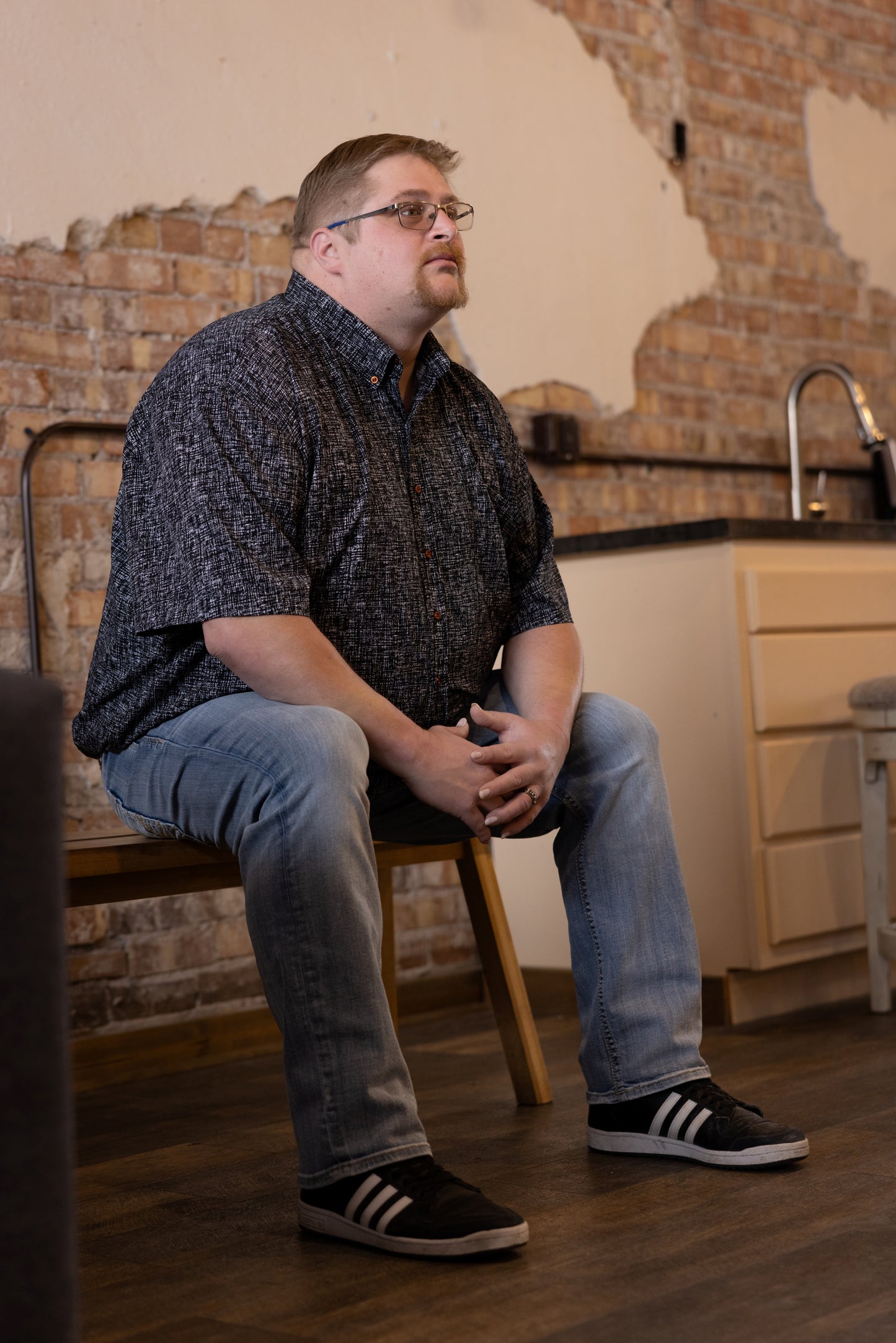 Man sitting on a chair in a kitchen with brick walls and wooden floor.